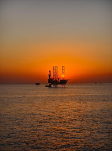 Silhouette of an offshore oil rig against a vivid sunset over tranquil waters.