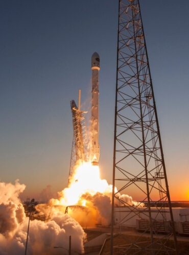 Low angle of modern rocket taking off into cloudless sky during beautiful sunset over space factory